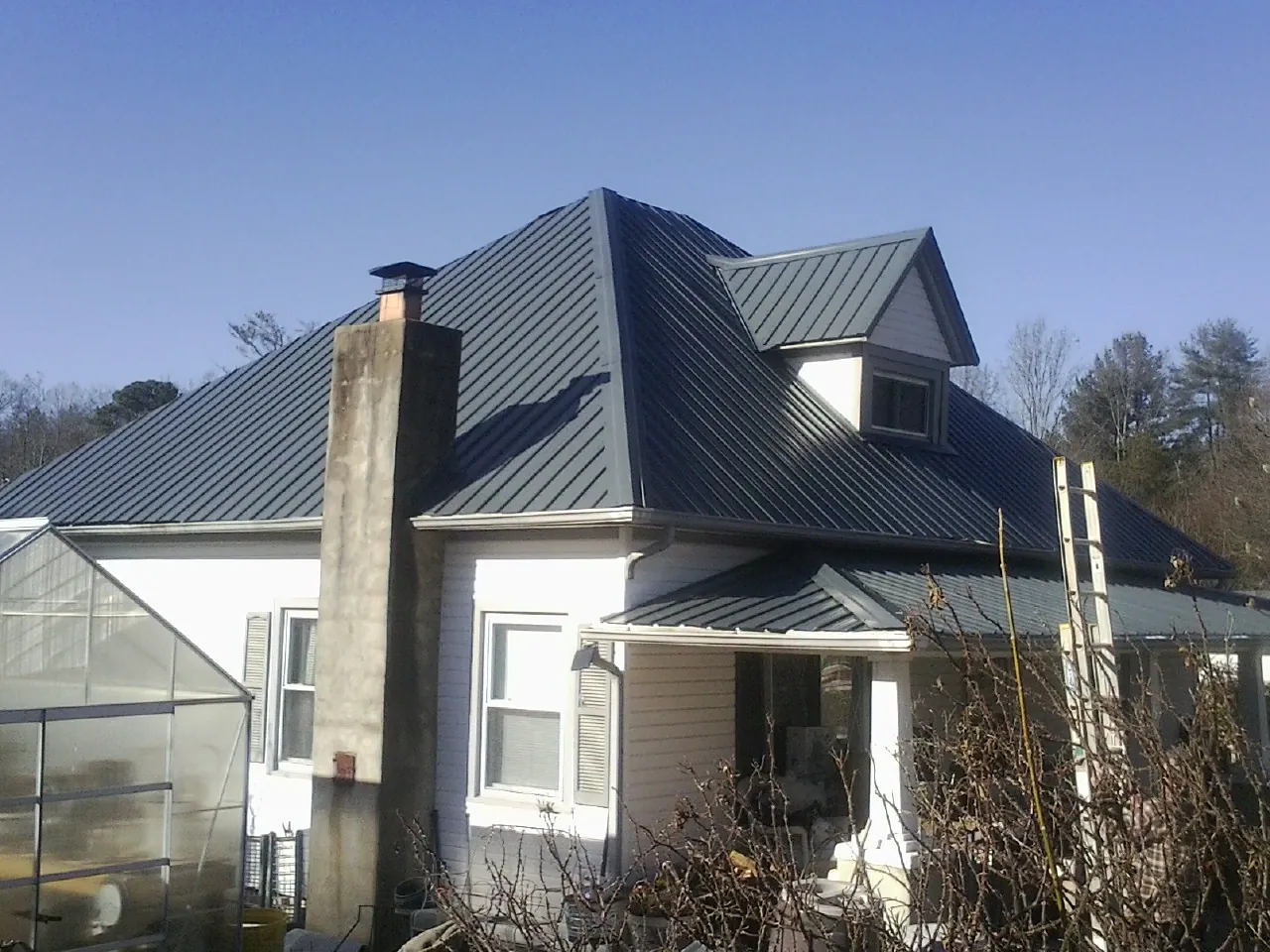 Dark blue standing seam metal roof on a white farmhouse with dormer — Slate & Tile Roof Repair by Roofing Brothers in Spring Hill