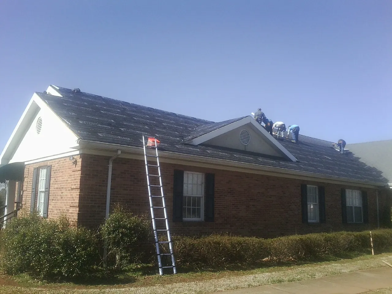 Crew tearing shingles off a brick ranch roof with a ladder set — Metal Roof Repair work by our crew in Spring Hill