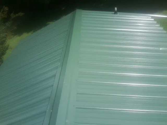 New green metal panels meeting at the ridge of a roof — Flat Roof Repair work by our crew in Spring Hill